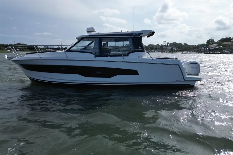 Slide: The Image of 2026 Jeanneau NC 1095 Coupe boat on water, side view, under cloudy sky. - 48
