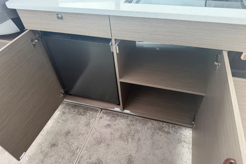 Slide: The Image of Interior view of Jeanneau NC 1095 Coupe 2026, featuring open wooden cabinets and a compact fridge. - 97