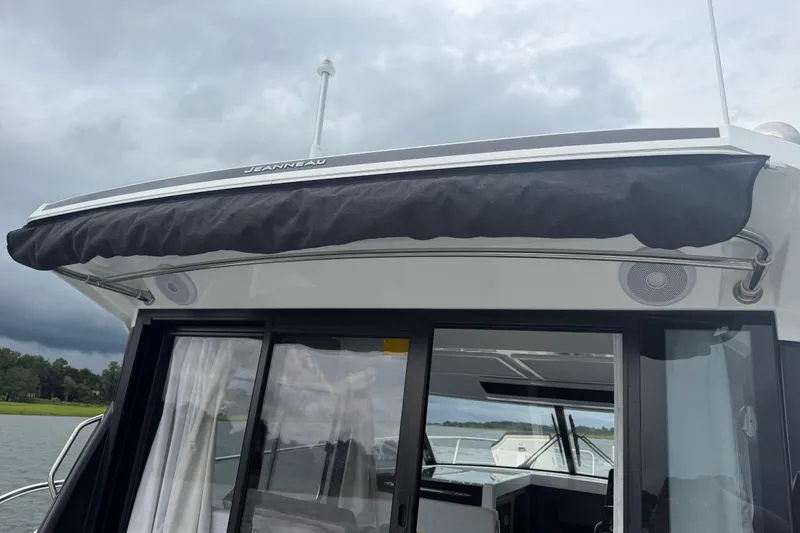 Slide: The Image of 2026 Jeanneau NC 1095 Coupe boat with black canopy, docked under cloudy skies. - 84