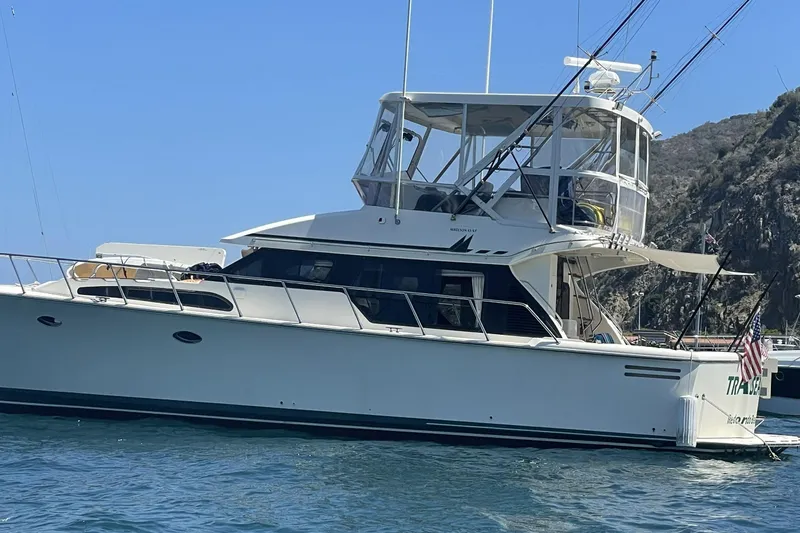 Slide: The Image of 1998 Mikelson 43 Sportfisher yacht anchored near rocky coastline under clear blue sky. - 2