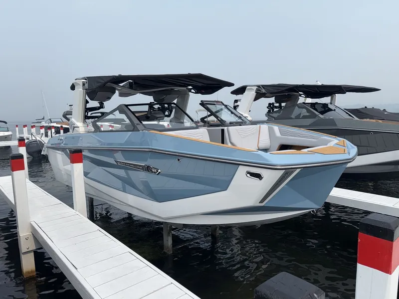 Slide: The Image of A modern Nautique G23 boat from 2027 docked. It features a sleek blue and white design. - 8