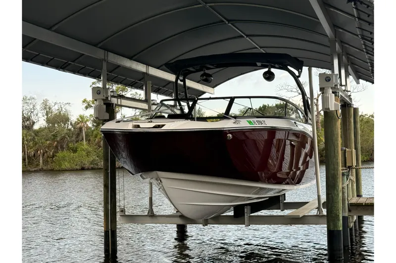 Slide: The Image of 2022 Yamaha Boats 252SD on lift, docked by a scenic river under a covered structure. - 2