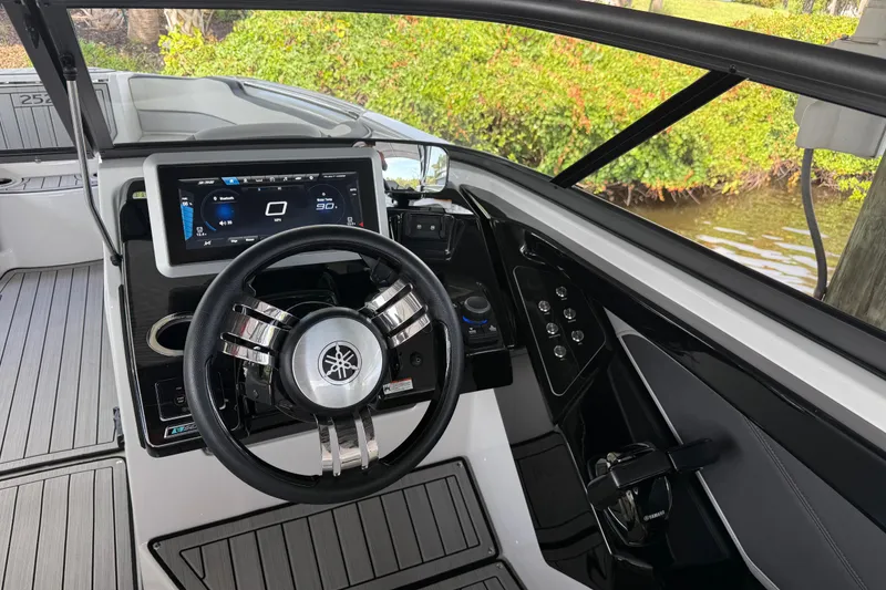 Slide: The Image of 2022 Yamaha Boats 252SD helm with modern dashboard and steering wheel, docked by lush greenery. - 36