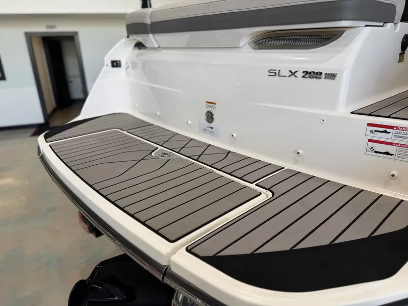 Slide: The Image of The image shows the stern of a 2024 Sea Ray SLX 260 Surf boat with a gray deck. - 12