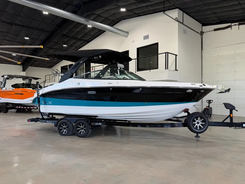 The Image of A 2024 Sea Ray SLX 260 Surf boat on a trailer inside a showroom. - 1