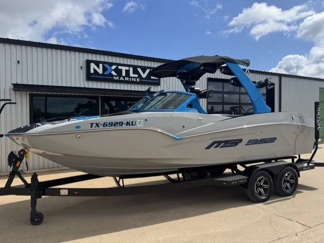 Slide: The Image of A 2023 MB SPORTS B52 23 Alpha boat on a trailer in front of a building. - 2