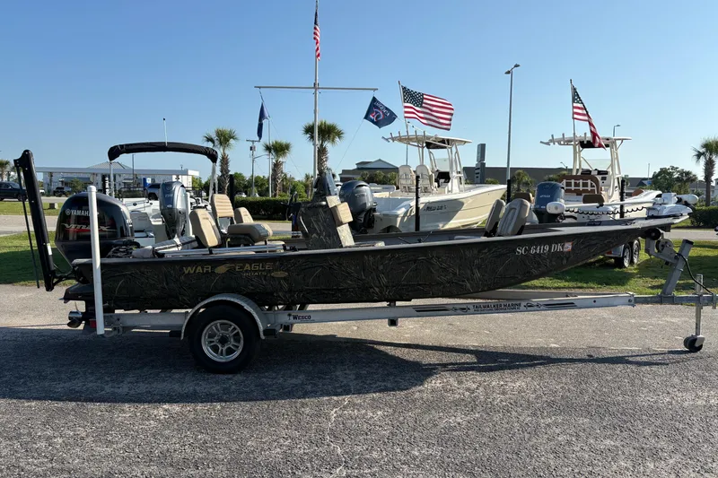 Slide: The Image of 2019 War Eagle 961 Blackhawk boat on trailer, parked outdoors with flags in background. - 3