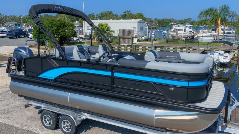 Slide: The Image of Bennington 21 S Swingback 2027: Sleek pontoon boat with blue accents, on a trailer by the water. - 3
