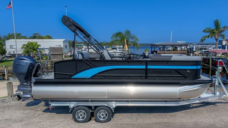 The Image of A Bennington 21 S Swingback pontoon boat on a trailer, featuring a blue and black design with an outboard motor. - 1