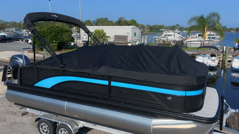The Image of Bennington 21 S Swingback 2027 on a trailer, with black and blue cover, in a marina. - 1