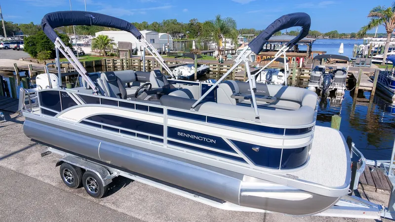 Slide: The Image of A sleek Bennington pontoon boat with blue and gray accents, parked on a trailer at the marina. - 4