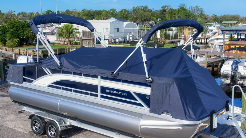 Slide: The Image of A 2027 Bennington 22 S Swingback pontoon boat with a blue cover on a trailer. - 23