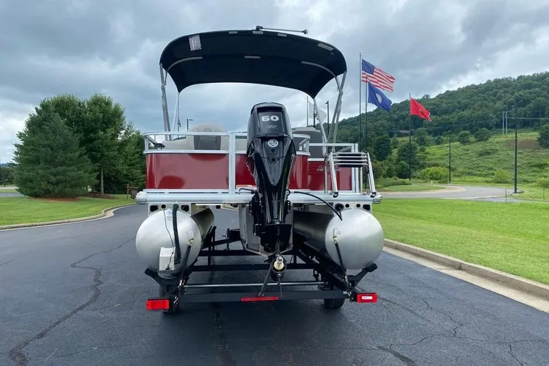 Slide: The Image of 2026 Sun Tracker Bass Buggy 18 DLX pontoon boat on trailer, flags in background. - 3
