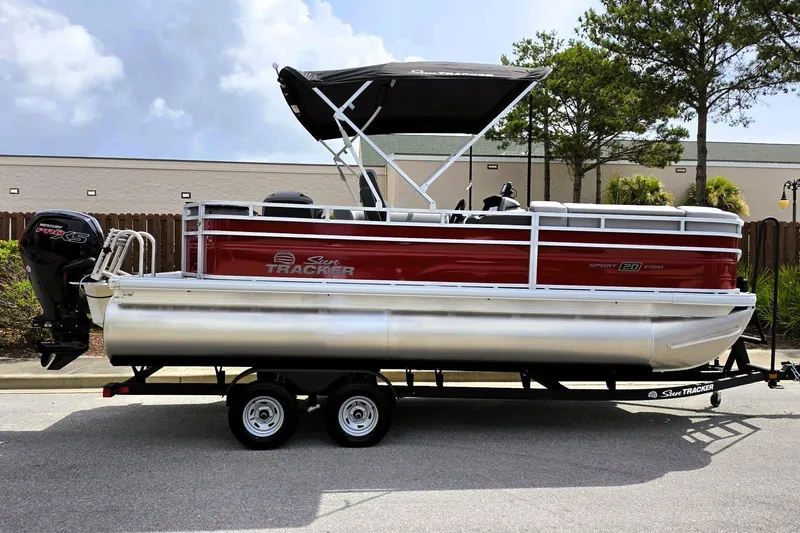 The Image of 2026 Sun Tracker SportFish 20 DLX pontoon boat on trailer, featuring red and silver design. - 0