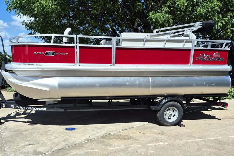 The Image of 2026 Sun Tracker Bass Buggy 18 DLX pontoon boat on trailer, red and silver design. - 0