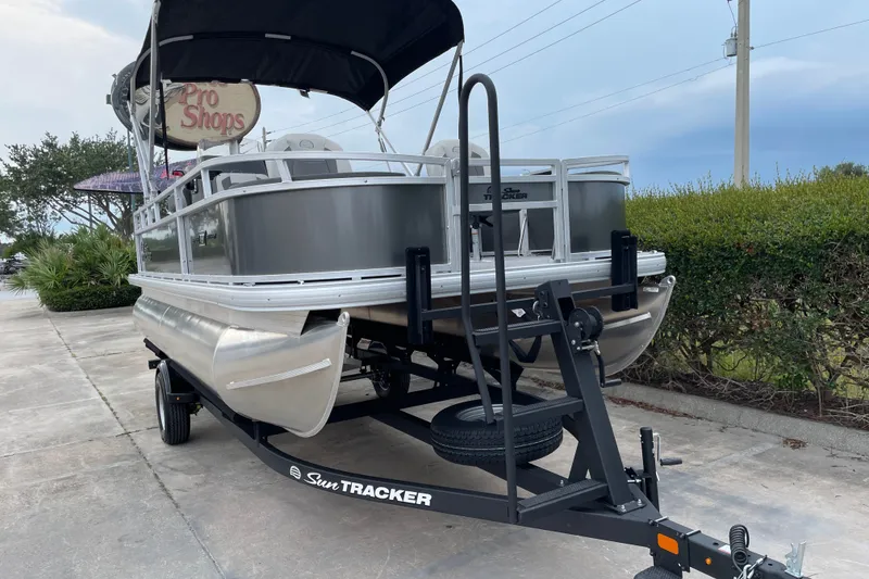 Slide: The Image of 2026 Sun Tracker Bass Buggy 18 DLX pontoon boat on trailer, parked outdoors. - 5