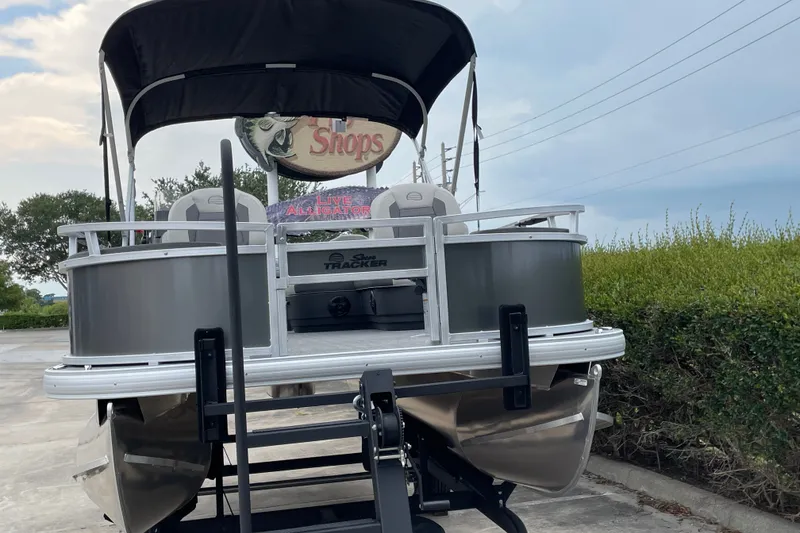 Slide: The Image of 2026 Sun Tracker Bass Buggy 18 DLX pontoon boat on trailer, parked outdoors. - 6