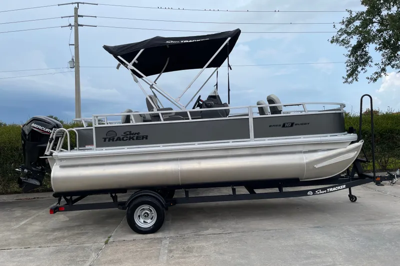 Slide: The Image of 2026 Sun Tracker Bass Buggy 18 DLX pontoon boat on trailer, parked outdoors. - 4