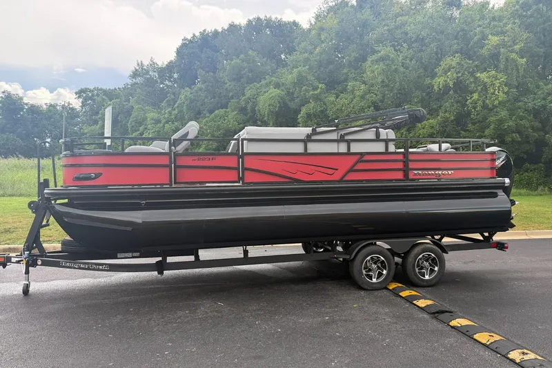 The Image of 2026 Ranger 223F pontoon boat on trailer, parked near lush greenery. - 0