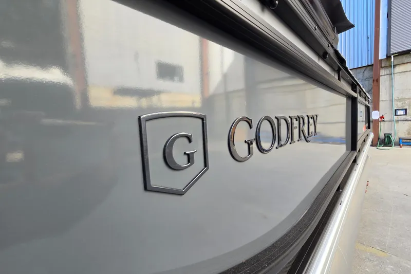 Slide: The Image of 2024 Godfrey Sweetwater 2486 SB boat with logo detail in a marina setting. - 6