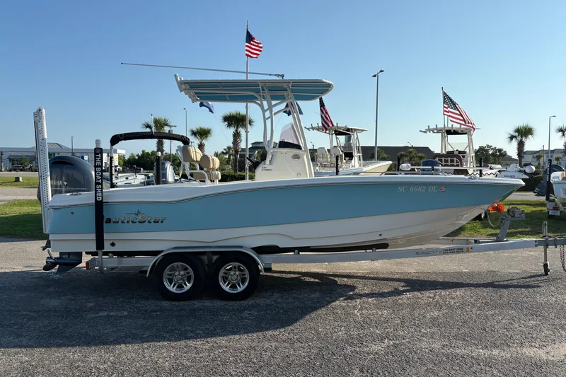 Slide: The Image of 2019 NauticStar 231 Hybrid boat on trailer, displayed outdoors with flags. - 3