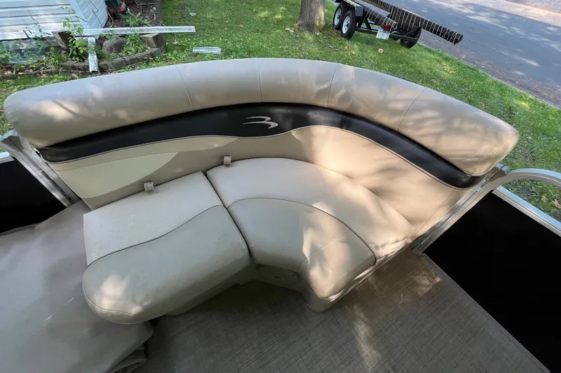 Slide: The Image of 2016 Bennington SX 20 boat seating with beige and black upholstery, parked near a grassy area. - 18