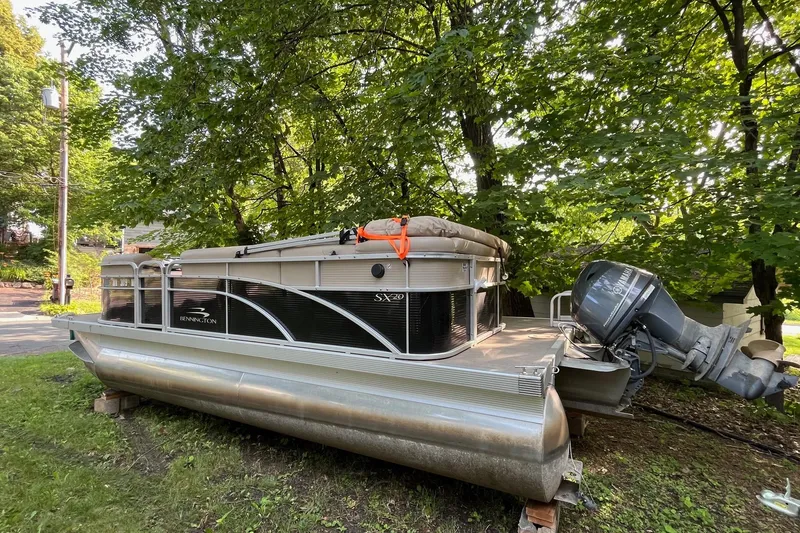 Slide: The Image of 2016 Bennington SX 20 pontoon boat parked on grass under trees. - 2