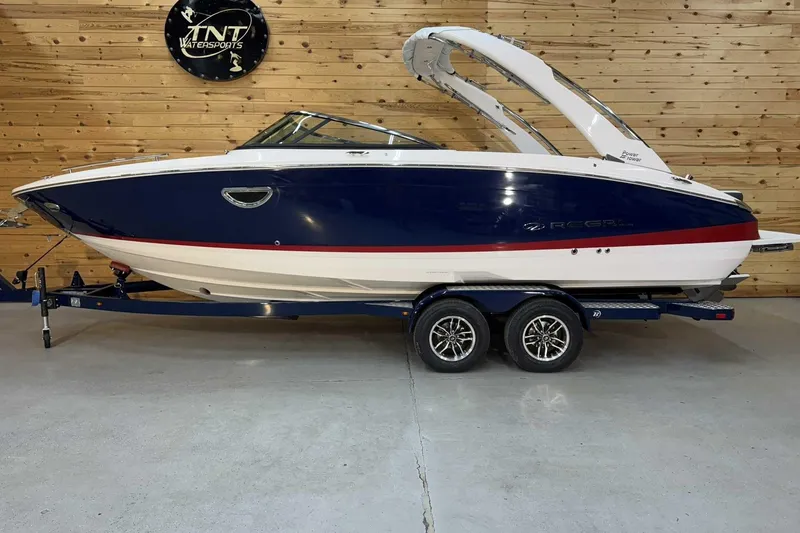 The Image of 2025 Regal LS6 boat with blue and white design on a trailer indoors. - 1