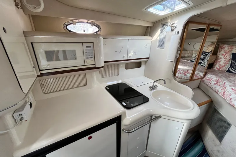 Slide: The Image of 1995 Sea Ray Sundancer 330 interior with kitchenette, featuring microwave, sink, and cozy sleeping area. - 14