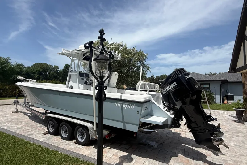 Slide: The Image of 1995 Intrepid 323 Open boat with Suzuki engine on a trailer in a driveway. - 74