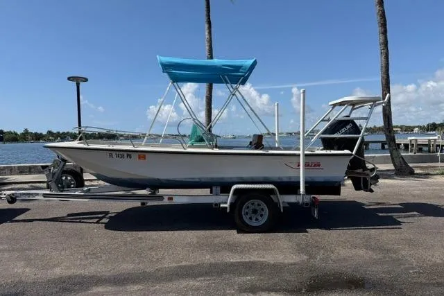 The Image of 1990 Boston Whaler 17 Newport boat on trailer by waterfront, featuring blue canopy. - 1