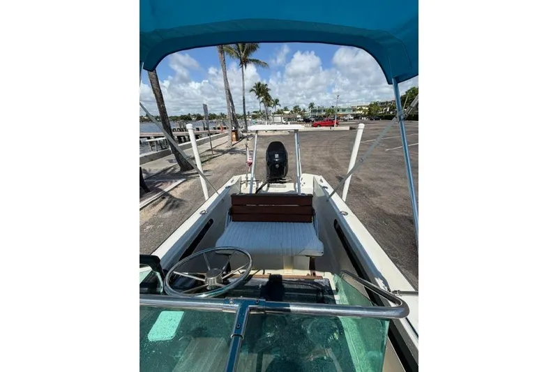 Slide: The Image of 1990 Boston Whaler 17 Newport boat with blue canopy, docked near palm trees. - 9