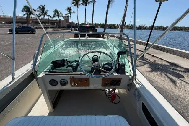 Slide: The Image of 1990 Boston Whaler 17 Newport boat interior with steering wheel, docked near palm trees and water. - 6