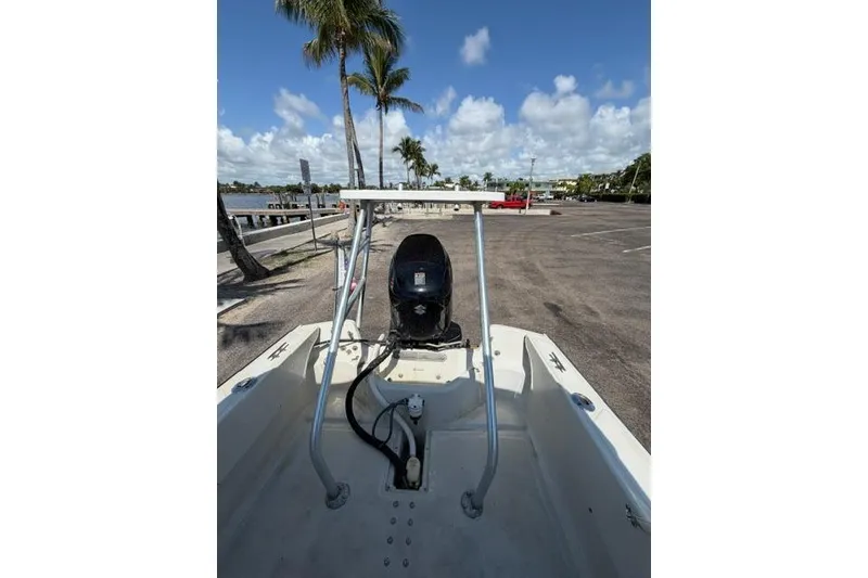 Slide: The Image of 1990 Boston Whaler 17 Newport boat with outboard motor, parked near waterfront under palm trees. - 10