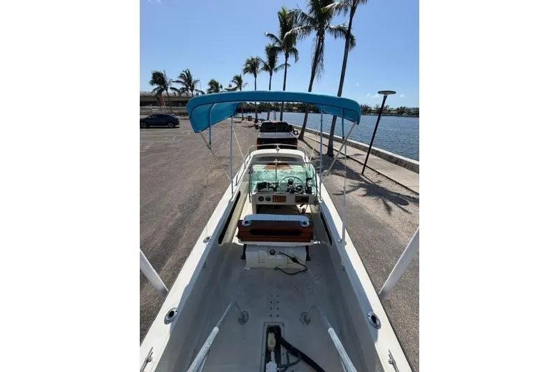 Slide: The Image of 1990 Boston Whaler 17 Newport boat with blue canopy, parked near waterfront and palm trees. - 11