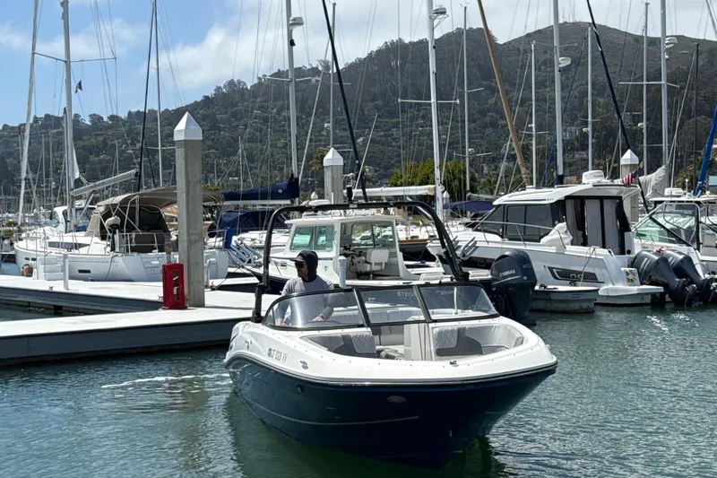 Slide: The Image of 2021 Bayliner VR5 Bowrider I/O navigating marina, surrounded by docked boats and scenic hills. - 10