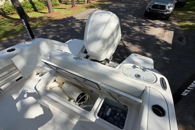 Slide: The Image of 2019 Edgewater 230CC boat interior with open storage compartments and motor, parked outdoors. - 26