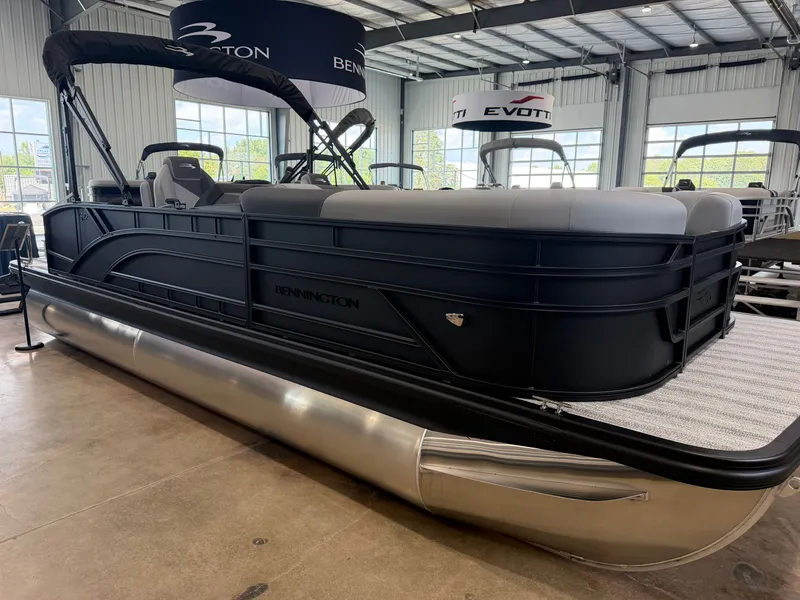 Slide: The Image of A sleek pontoon boat with a black hull and gray seating in a showroom. - 3