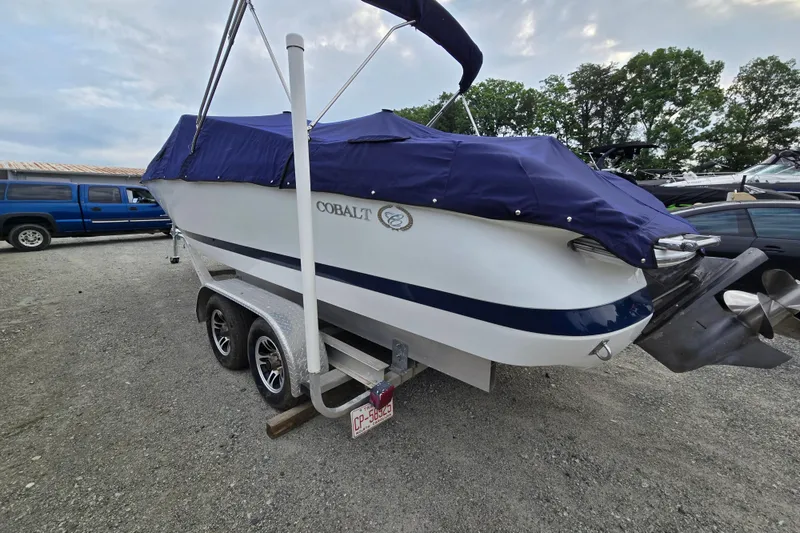 Slide: The Image of Covered 2000 Cobalt 246 boat on trailer, parked outdoors with trees in background. - 3