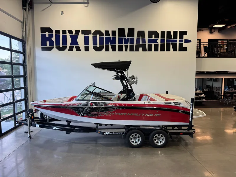 The Image of A 2011 Super Air Nautique 210 boat on a trailer in a showroom. - 1