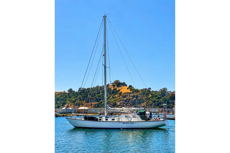 Slide: The Image of Custom Steel Cutter sailboat from 1987 on a sunny day, docked near a scenic hillside. - 1