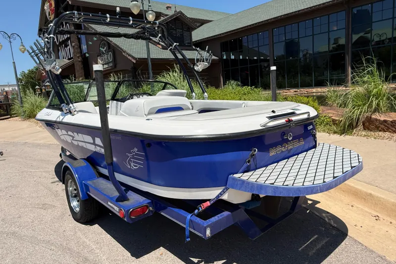 Slide: The Image of 2001 Moomba Outback boat with blue hull, parked on a trailer near a building. - 5