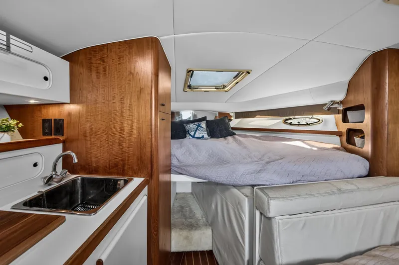 Slide: The Image of 1995 Tiara Yachts 3100 Open interior with cozy bed, wooden cabinetry, and compact kitchenette. - 11