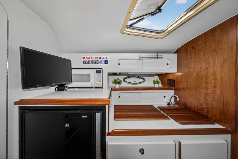 Slide: The Image of Interior of 1995 Tiara Yachts 3100 Open, featuring kitchenette with microwave, sink, and TV. - 10