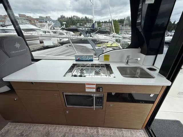 Slide: The Image of The 2021 Jeanneau NC 1095 galley features a stove, sink, and microwave. - 12
