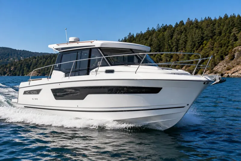 The Image of A 2021 Jeanneau NC 1095 boat cruising on calm waters, surrounded by forested hills. - 0