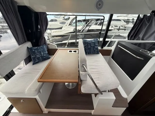 Slide: The Image of Interior of the Jeanneau NC 1095 featuring a table and benches, surrounded by windows overlooking other boats. - 8