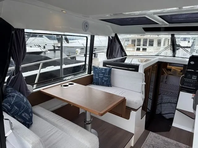 Slide: The Image of Interior of Jeanneau NC 1095 with table, benches, and windows overlooking the marina. - 4