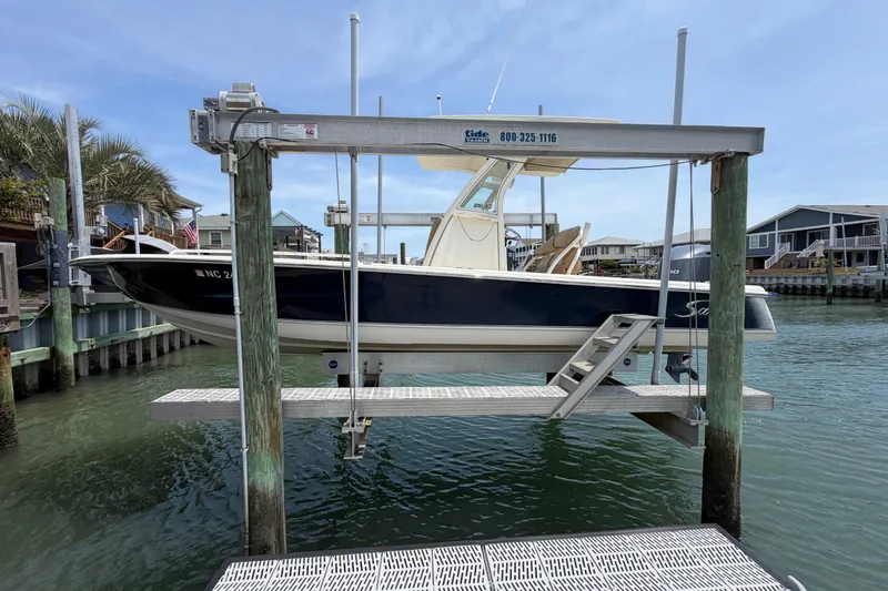 The Image of 2012 Scout 251 XS boat on lift at marina, surrounded by water and docks. - 0