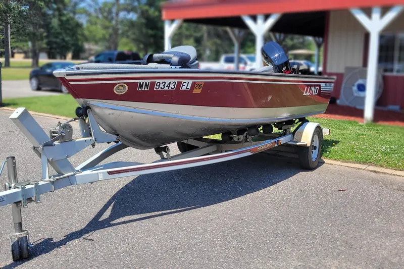 The Image of 1989 Lund 1600 Stinger boat on trailer, parked outdoors near a building. - 1